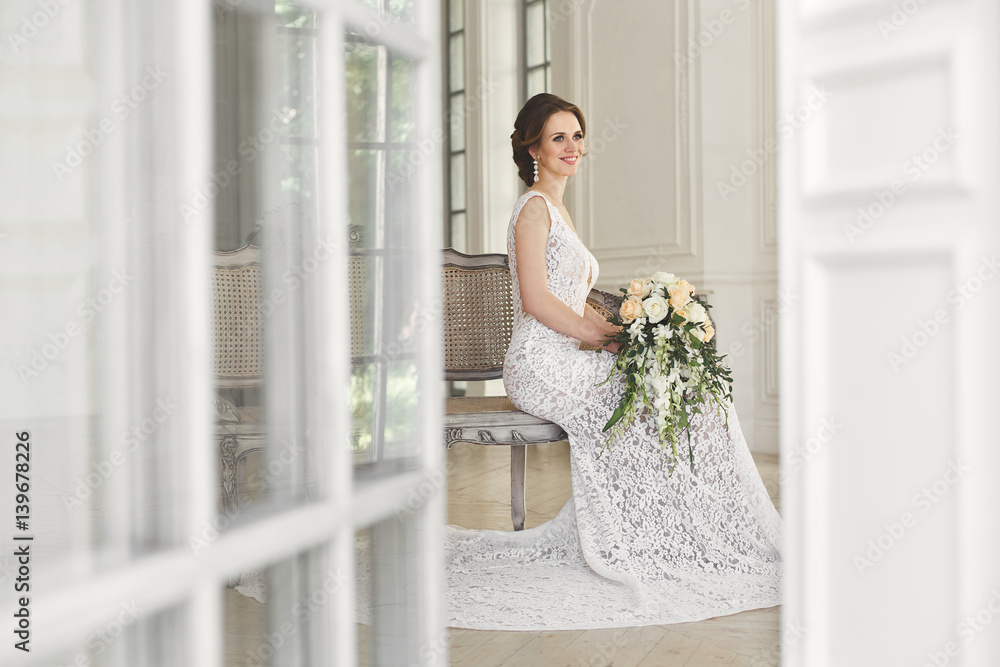 Beautiful bride posing in wedding dress in a white photo Studio. Mirror. Sofa. Bouquet. The door. Chandelier. Beautiful bride posing in wedding dress in a white photo Studio. Mirror. Sofa. Bouquet. The door. Chandelier.