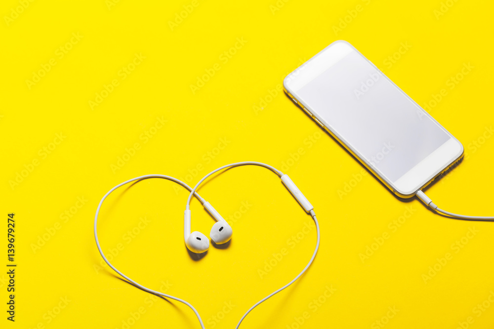Close-up of smart phone with headphones on a yellow background. (Top view). Listen to music. Close-up of smart phone with headphones on a yellow background. (Top view). Listen to music.