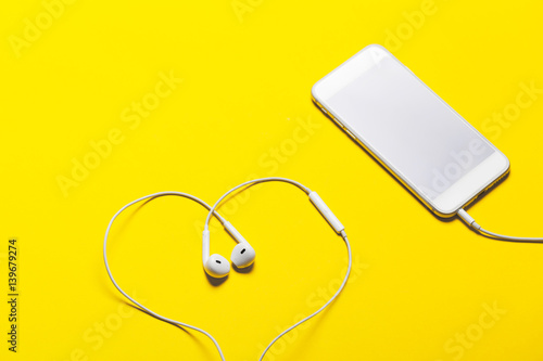 Close-up of smart phone with headphones on a yellow background. (Top view). Listen to music.