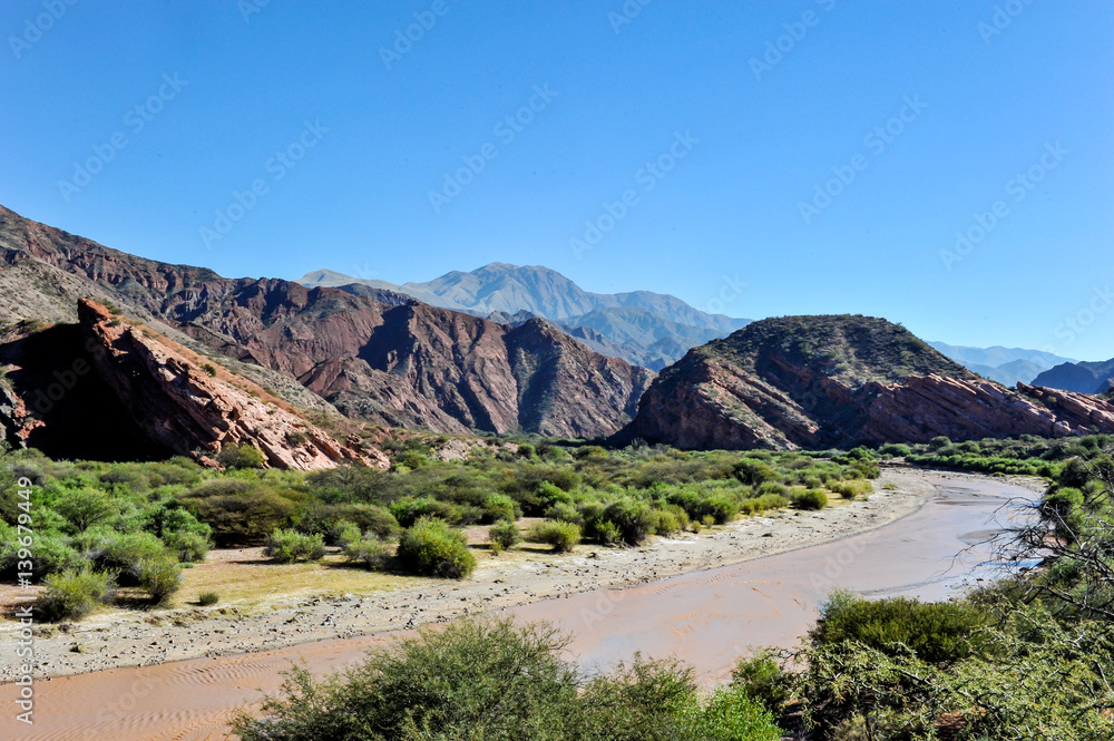 River at coloured rock mountains. Hill of Seven Colors over Purmamarca village. Quebrada de Humahuaca valley, a UNESCO World Heritage Site, Argentina. River at coloured rock mountains. Hill of Seven Colors over Purmamarca village. Quebrada de Humahuaca valley, a UNESCO World Heritage Site, Argentina.