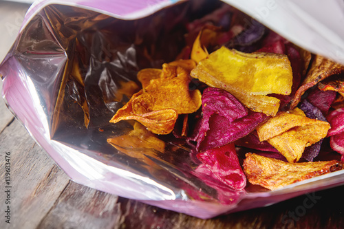 Beet and carrot salty chips in the bag from the store. Wooden dark background.