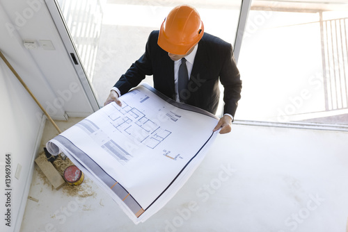 Man in suit wearing hard hat looking at blueprint photo