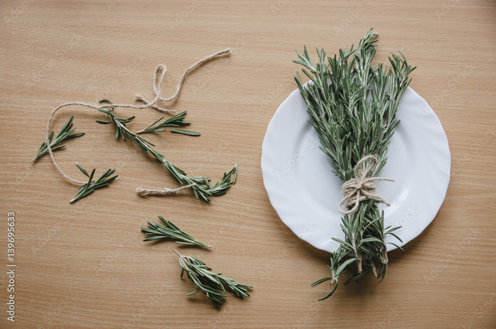 Rosemary on a white plate on a wooden background Rosemary on a white plate on a wooden background