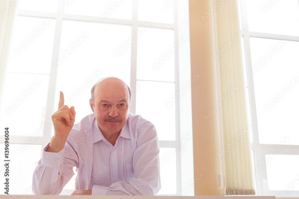 Man in white shirt stands near big window.