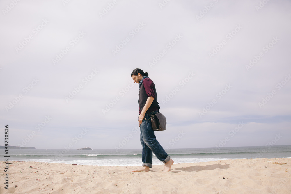 caucasian hipster man walking alone on the beach with casual clothes