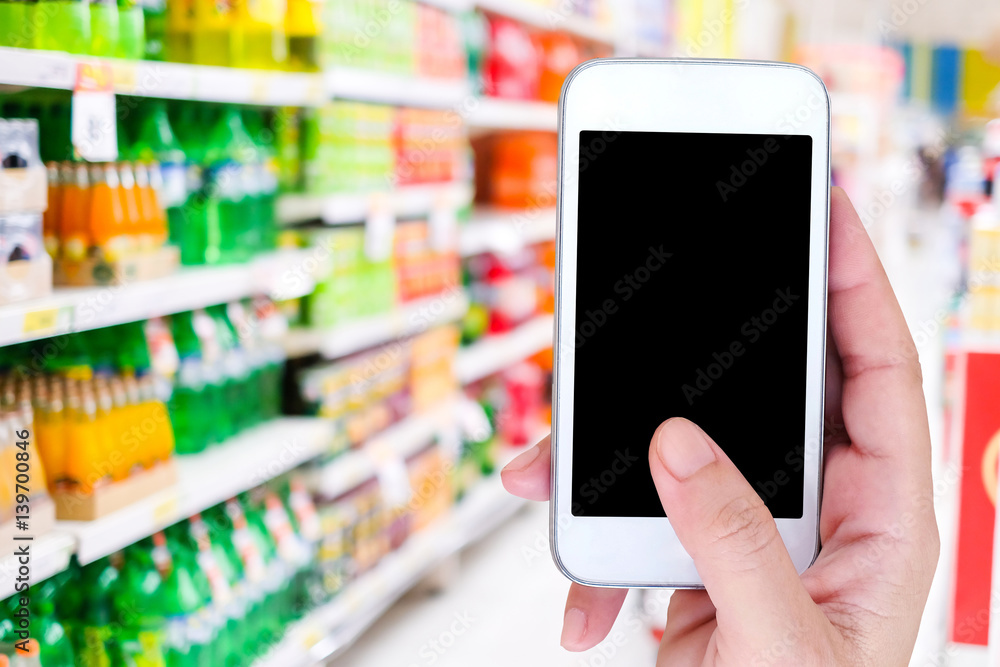 Hand holding smart phone with blank screen on blur supermarket background, mock up, template, business and technology, grocery online, digital marketing concept Hand holding smart phone with blank screen on blur supermarket background, mock up, template, business and technology, grocery online, digital marketing concept