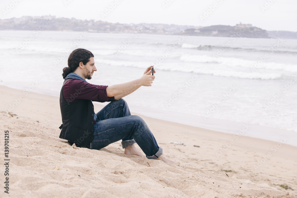 young man taking pictures with his phone isolated on the beach