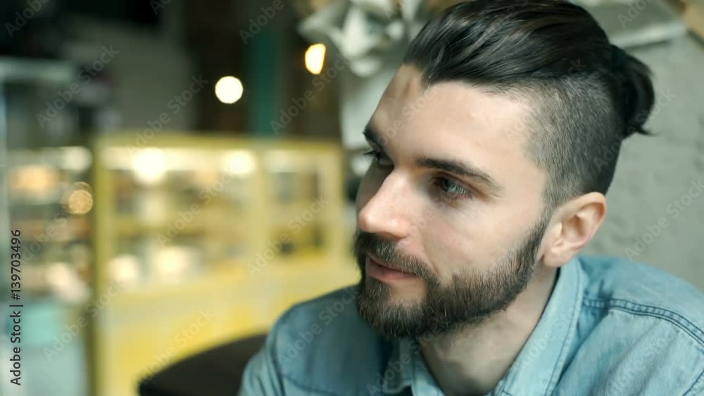Handsome man with bro bun sitting in the cafe and smiling to the camera
Handsome man with bro bun sitting in the cafe and smiling to the camera