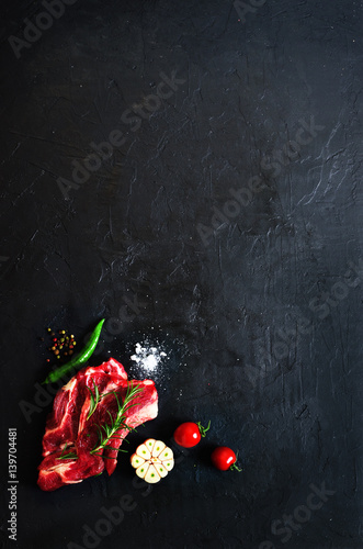 Raw fresh meat steak with cherry tomatoes, hot pepper, garlic, oil and herbs on dark stone, concrete background. Free space for your text