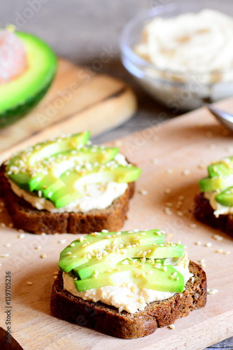 Healthy avocado and hummus sandwiches on a wooden board. Vegetarian open sandwiches. Lenten menu. Vertical photo. Closeup
