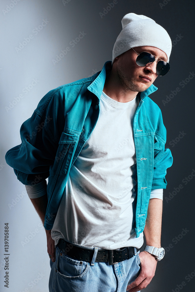 Male fashion concept. Fashionable young man wearing trendy posing over gray background. Hands in pockets, crossed legs. Street style. Studio shot Male fashion concept. Fashionable young man wearing trendy posing over gray background. Hands in pockets, crossed legs. Street style. Studio shot