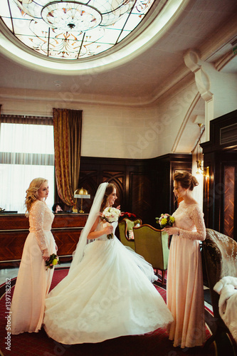 Bridesmaids in pink dresses stand with bride in luxury room
