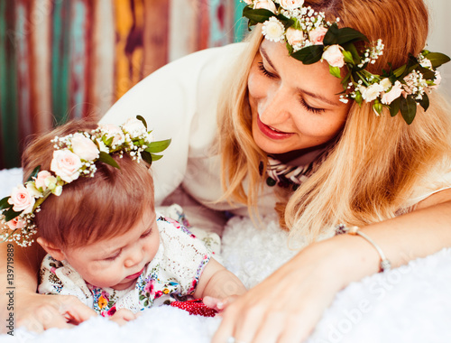 Woman in flower wreath plays with her little daughter on flyffy blanket photo