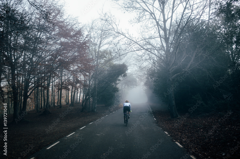 Fototapeta premium A silhouette of a cyclist riding in the foggy and misty forest road