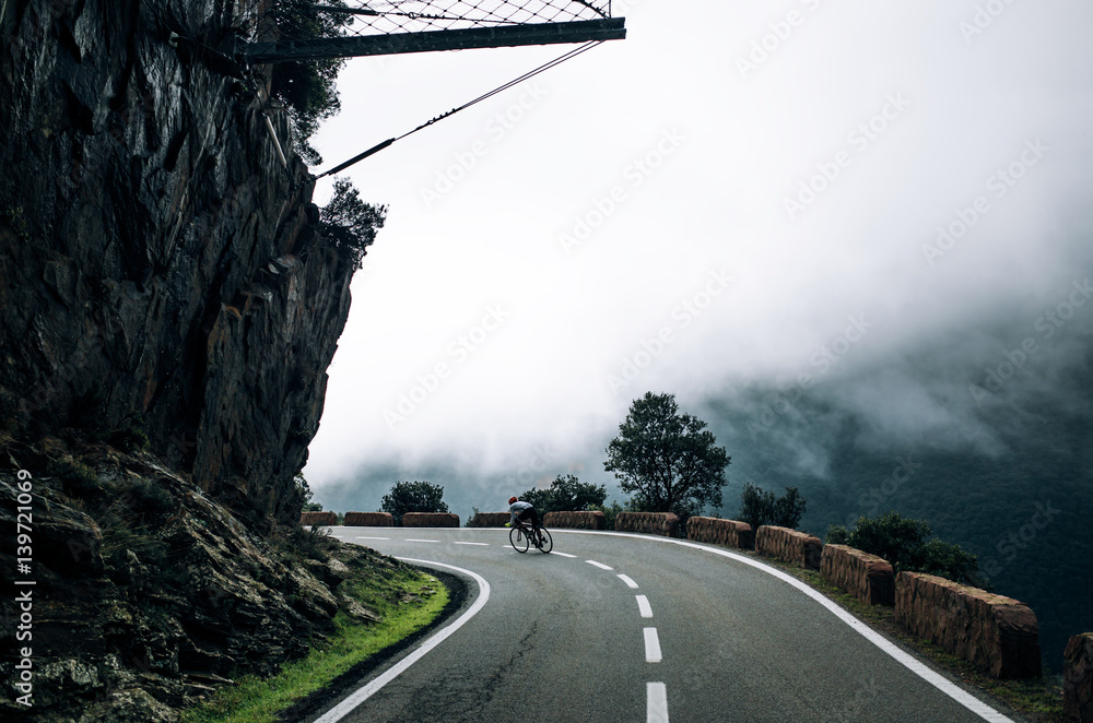 Fototapeta premium A wide shot of a male cyclist riding a dark and gloomy mountain road
