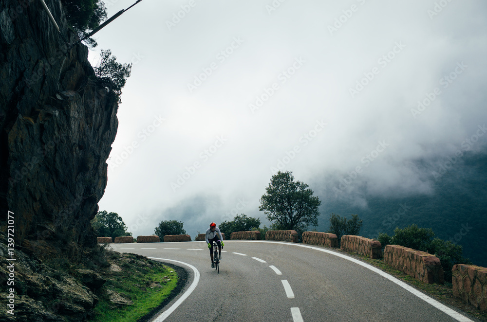 Obraz premium A shot of a cyclist riding towards the camera on the mountain road above the clouds