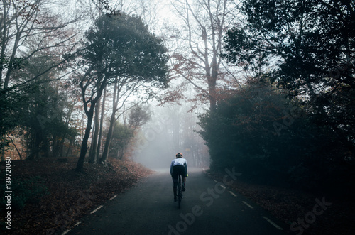 A professional male cyclist riding his bike in a dark autumn forest in the fog