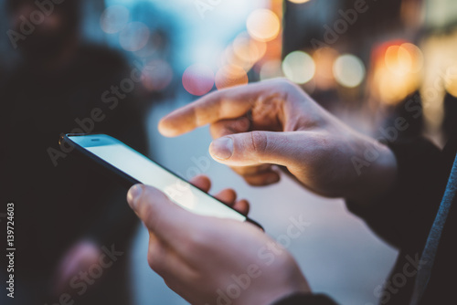 Closeup of male hands using modern smartphone with blank screen with copy spce for design or text message, hipster guy walking in the city and looking for bar or restaurant via an app on cellphone