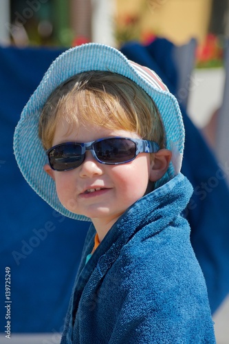 adorable toddler boy wrapped in towl wearing sunglasses sunhat sitting outside on vacation 