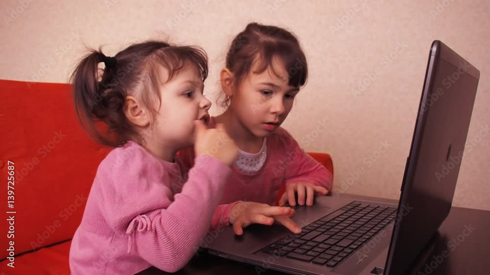 Children playing in the laptop. Two little girls are printed on a laptop. Two sisters sitting on the orange couch looking at a laptop. Children playing in the laptop. Two little girls are printed on a laptop. Two sisters sitting on the orange couch looking at a laptop.