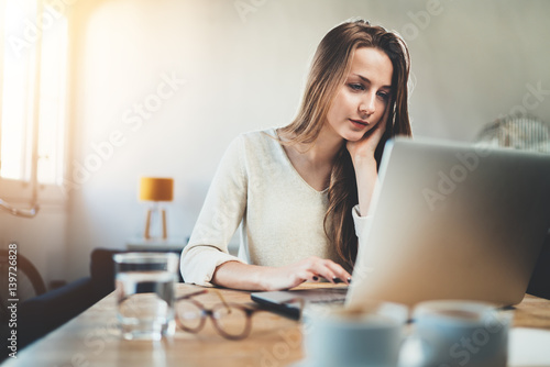 Attractive young woman using laptop while working at home interior  casual style  long hours at work  pretty female student using portable computer at coffee shop