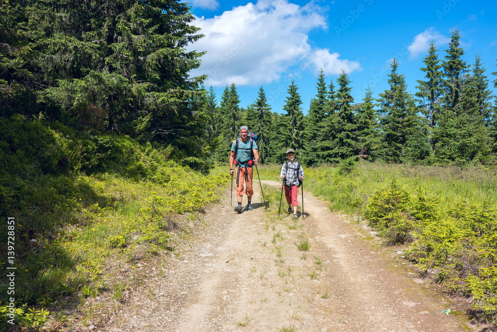 Father and son with backpacks walk along the road Father and son with backpacks walk along the road