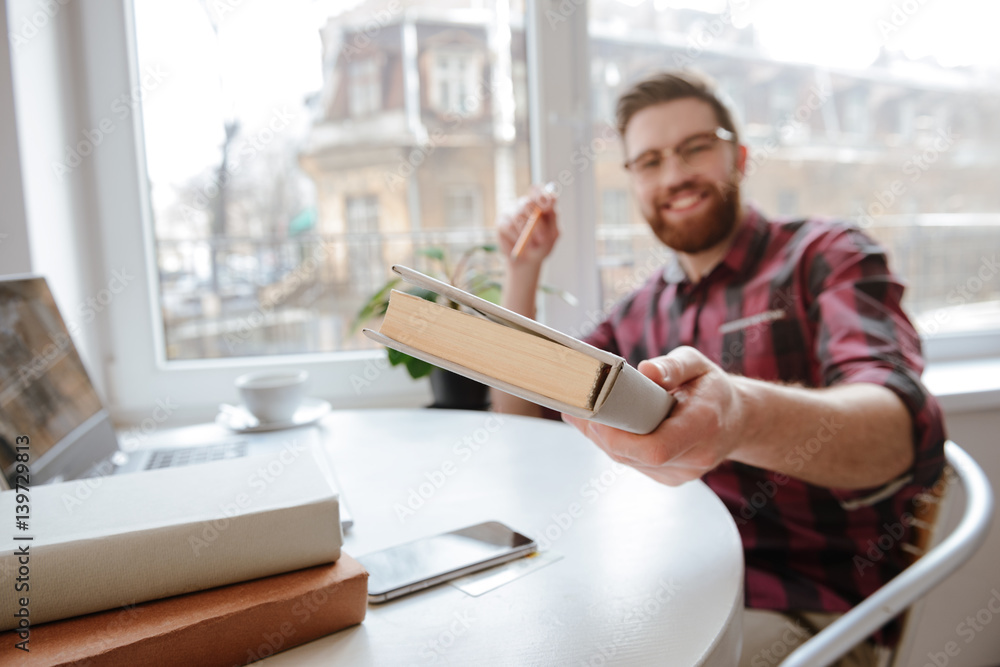 Happy bearded man showing book to camera. Focus on book. Happy bearded man showing book to camera. Focus on book.