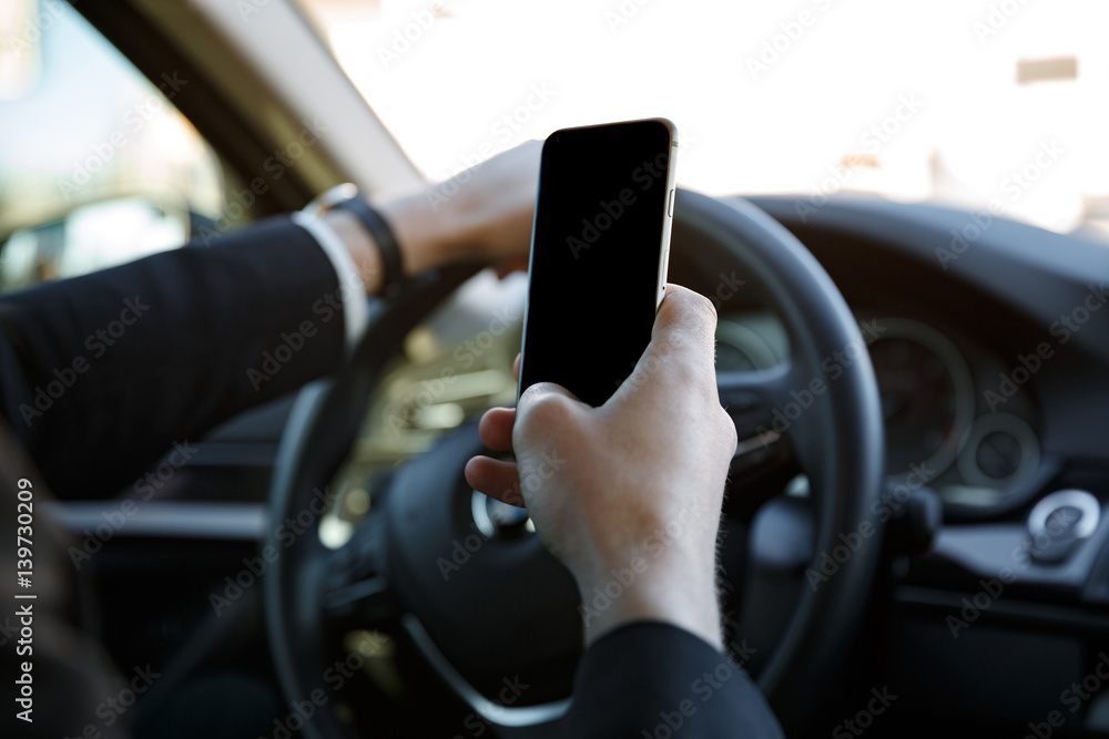 Man in suit driving car and holding mobile phone