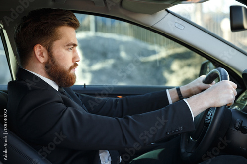 Serious bearded business man driving car