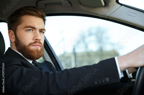 Serious bearded business man driving car