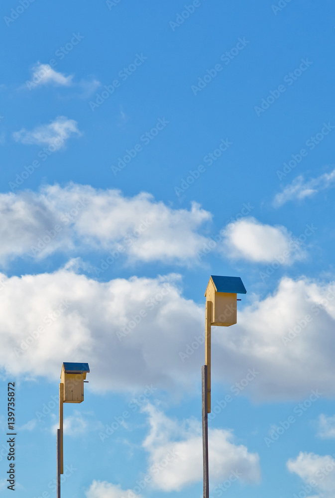 Two yellow birdhouses on the blue sky background Two yellow birdhouses on the blue sky background