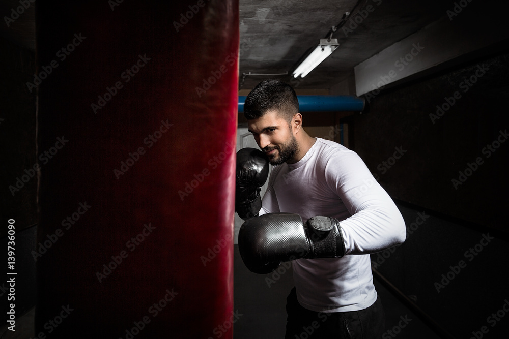 Young sportsman practicing kickboxing punches with boxing gloves and punching bag at the gym