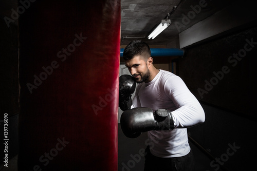 Young sportsman practicing kickboxing punches with boxing gloves and punching bag at the gym © bokan