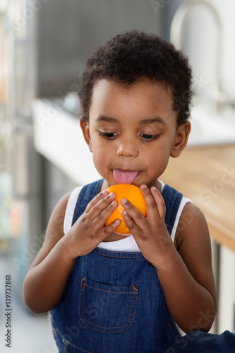 Petit garçon qui lèche une orange dans la cuisine