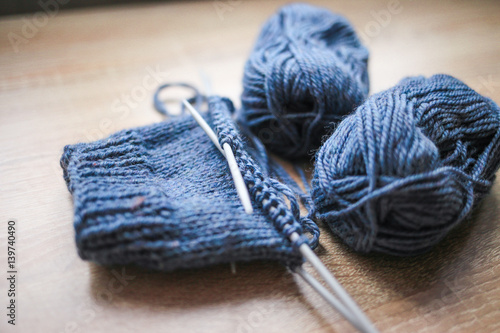 Knitting needles, loop counter and blue yarn are on the table. Wooden background. Hobbies 