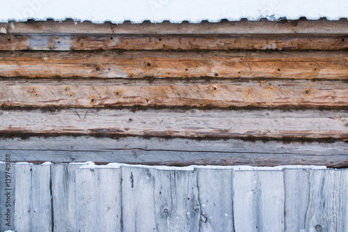 Background of wall with wooden logs with oakum, the roof with snow and wooden fence