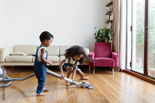 Une petite fille aide son petit frère à passer l'aspirateur dans le salon