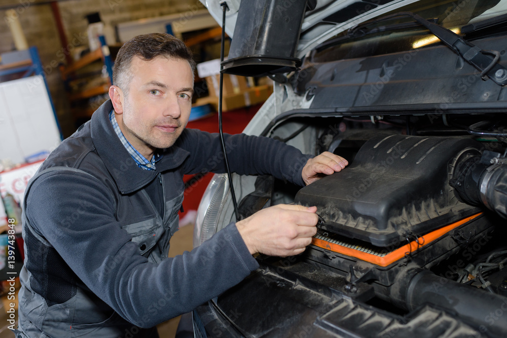 smiling mechanic repairing car engine in a garage smiling mechanic repairing car engine in a garage