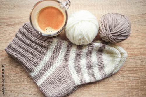 Beige and white yarn, beige-beige sock and black coffee are on the table. Wooden background. Hobbies 