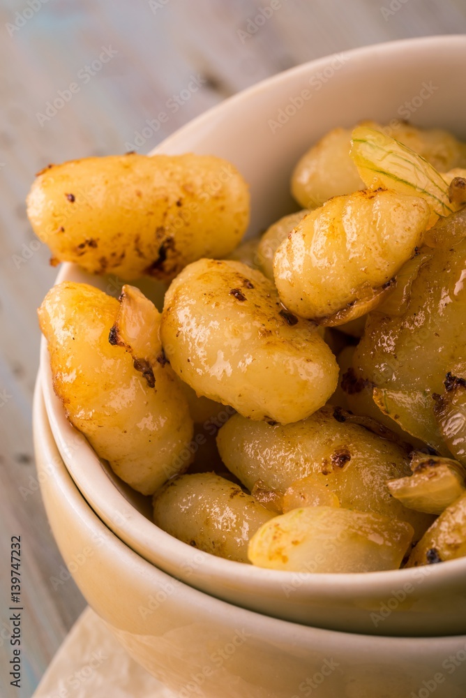Portion of fried gnocchi with onion in light bowl Portion of fried gnocchi with onion in light bowl