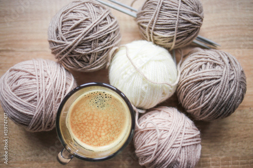 Coffee, knitting needles, beige and white yarn are on the table. Wooden background. Hobbies 