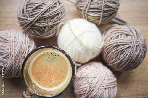 Coffee, knitting needles, beige and white yarn are on the table. Wooden background. Hobbies 