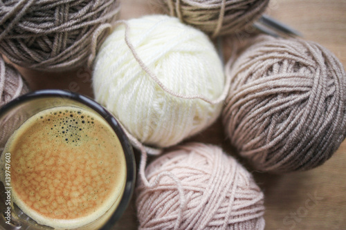 Coffee, knitting needles, beige and white yarn are on the table. Wooden background. Hobbies 