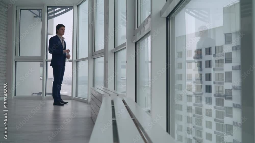 handsome businessman drinking water at home or in office looking on the street with urban landscape and high rise building. Successful entrepreneur holding bottle wearing in elegant suit. handsome businessman drinking water at home or in office looking on the street with urban landscape and high rise building. Successful entrepreneur holding bottle wearing in elegant suit.