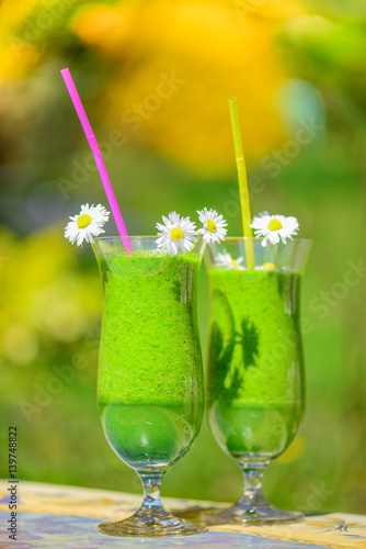 Zwei Gläser mit grünem Smoothie, dekoriert mit Gänseblümchen im Garten