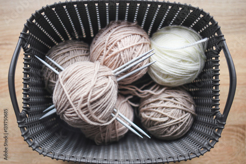 Beige, and white yarn, knitting needles in the grey basket. Wooden background. Knitting hobby