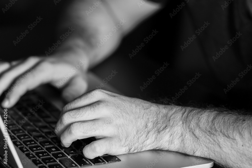 Man's hands are typing something on the laptop. Black and white photo