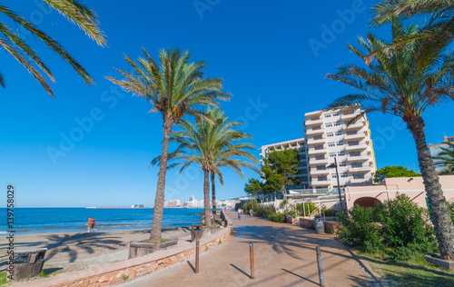 Ibiza sunshine on the waterfront in Sant Antoni de Portmany, Take a walk along the main boardwalk, now a stone concourse beside the beach. Places to stay in Ibiza. 