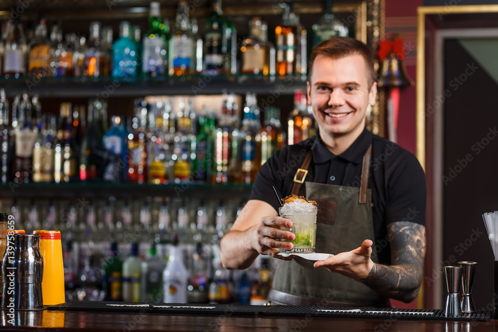 Cheerful bartender gives the cocktail to customer.