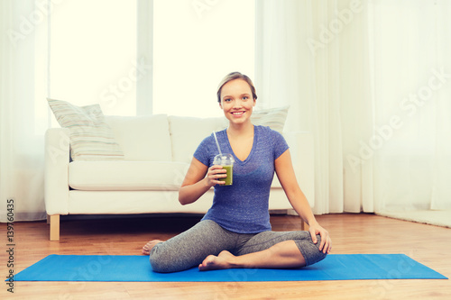 happy woman with smoothie sitting on mat at home